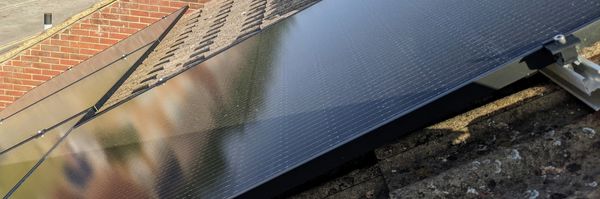 Four rectangular, dark blue, solar panels on a pale brown tiled roof.